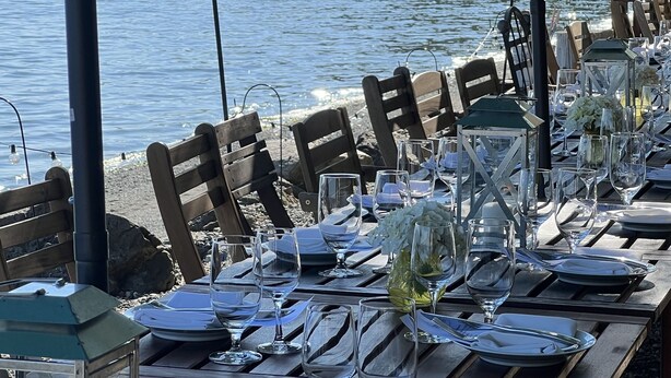 A table set for dining with clear glassware and plates, overlooking a body of water with a wooden deck and chairs. - 40 Acres Estate, Beach Access, Pet Friendly: Wildwood Studio (Vashon)