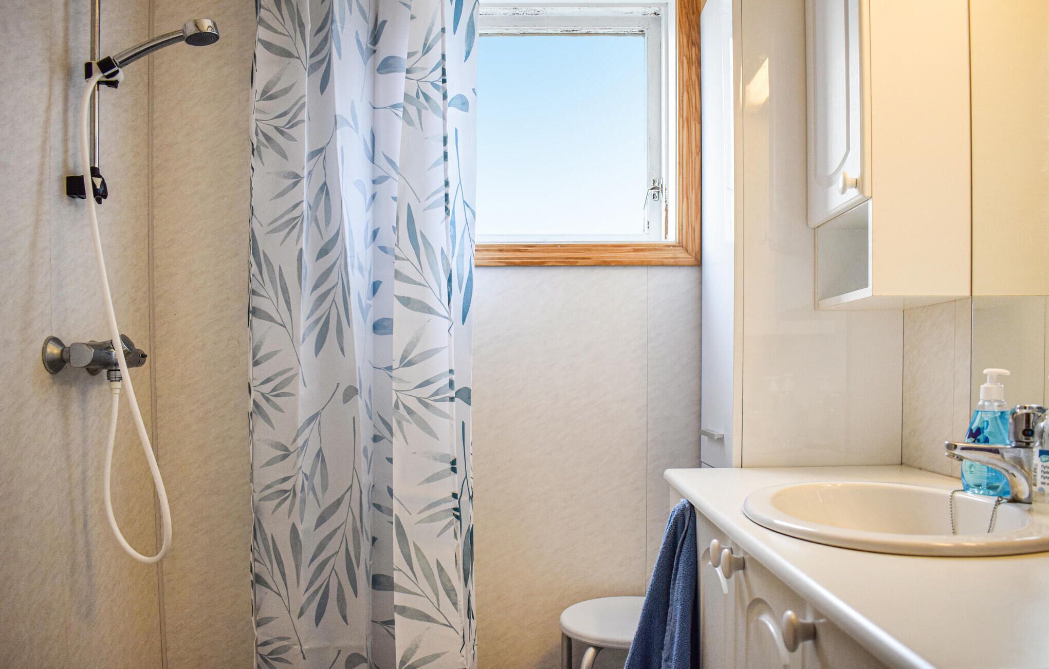 A bathroom with a shower, a sink, and a window.