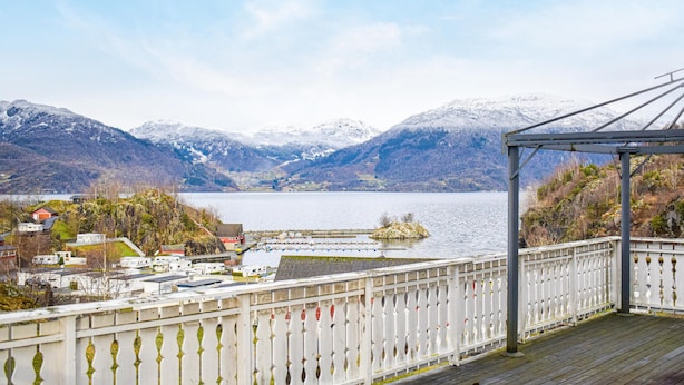 Blick auf ein Seeufer mit einer Holzterrasse, einem Pavillon und einer kleinen Insel im See.