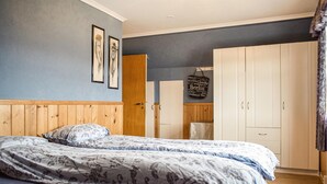 Ein Schlafzimmer mit einem hölzernen Kopfende, zwei Betten mit floralem Bettbezug, einem Kleiderschrank und einer Wand mit gerahmten Bildern.