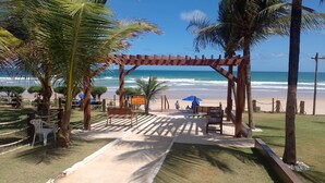 A beach entrance with a wooden pergola, palm trees, and a sign warning of strong currents. - Porto de Galinhas House in Cond. by the sea Esmeralda do Mar (Ipojuca)