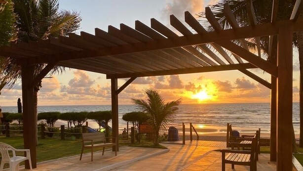 A wooden pergola with benches overlooking a beach at sunset. - Porto de Galinhas House in Cond. by the sea Esmeralda do Mar (Ipojuca)