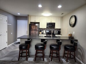 A modern kitchen with a central island, bar stools, and a microwave. - Great Location! Updated Condo with beautiful view of the channel & boat slip! (Osage Beach)
