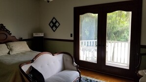 Ein Schlafzimmer mit Bett, Stuhl, Kommode und einem großen Fenster mit Balkonblick.