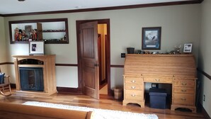 Ein Zimmer mit Kamin aus Holz, einem Spiegel, einer Tür zu einem weiteren Raum und einem Regal mit Spielzeug.