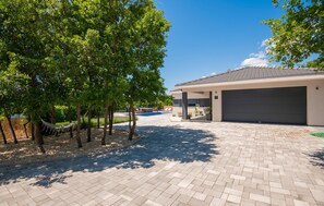 Une maison moderne dotée d’une allée pavée, d’une piscine et d’un patio couvert.