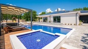 A swimming pool with a tiled deck, a covered seating area, and a modern house with solar panels. - Beautiful home in Glavina Gornja (Glavina Gornja)