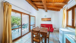 Ein Essbereich mit einem Holztisch und Stühlen, einem roten Sofa und Blick ins Freie durch eine Glastür.