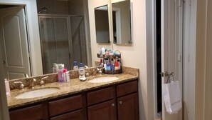 A bathroom with two sinks, a mirror, and a shower. There are toiletries on the countertop. - Waterfront Paradise condo (Bradenton)