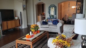 A living room with a sofa, coffee table, and TV. There is a kitchen in the background. - Waterfront Paradise condo (Bradenton)
