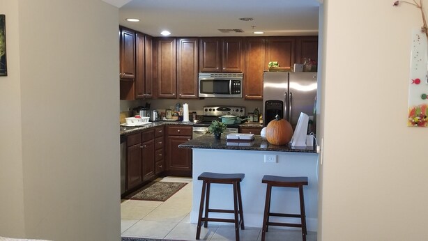 A kitchen with wooden cabinets, a stainless steel refrigerator, a microwave, and a sink. There are two stools at the island. - Waterfront Paradise condo (Bradenton)