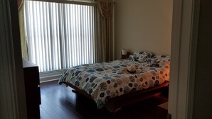 A bedroom with a bed, a nightstand, and a window with blinds. - Waterfront Paradise condo (Bradenton)