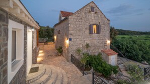 Un bâtiment en pierre doté d’un toit en pente, d’une petite fenêtre avec des volets et d’un chemin pavé menant à l’entrée.