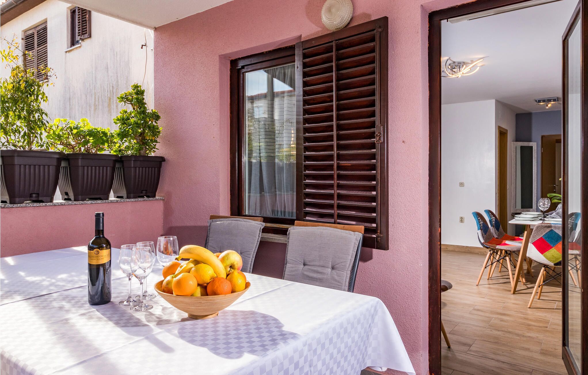 A dining area with a table set for two, a bottle of wine, and a bowl of fruit.