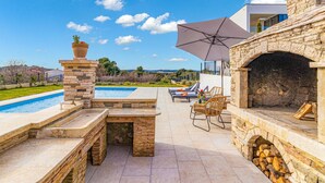 A poolside area with a stone fireplace, lounge chairs, and a large umbrella. - Nice apartment in Pula with house sea view (Pula)