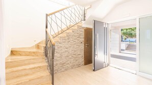 A modern staircase with wooden steps and metal railings, leading to a door with a stone wall behind it.