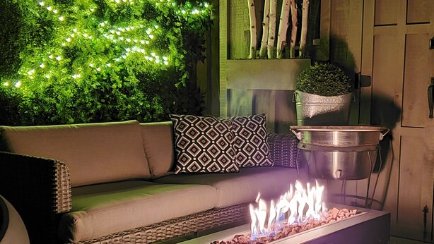 A cozy outdoor seating area with a green wall, a fire feature, and a hanging planter.