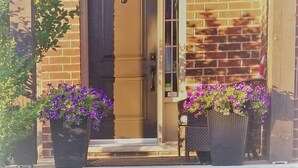 A brick building with a wooden door and a small porch with potted plants.