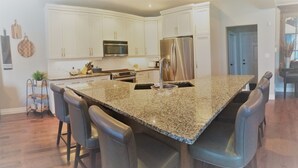 A modern kitchen with white cabinets, stainless steel appliances, and a granite island with bar stools.