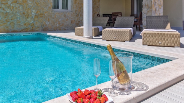 Un espace aménagé au bord de la piscine, avec un mur en pierre, des meubles en osier et une bouteille de champagne.