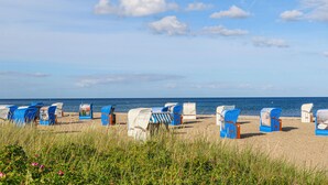A beach with rows of blue and white beach chairs and umbrellas, a sandy beach, and the ocean in the background. - Nice home in OstseeResort Olpenitz with sauna (OstseeResort Olpenitz)