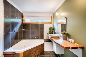 A modern bathroom with a freestanding bathtub, a wooden vanity, a large mirror, and a potted plant.