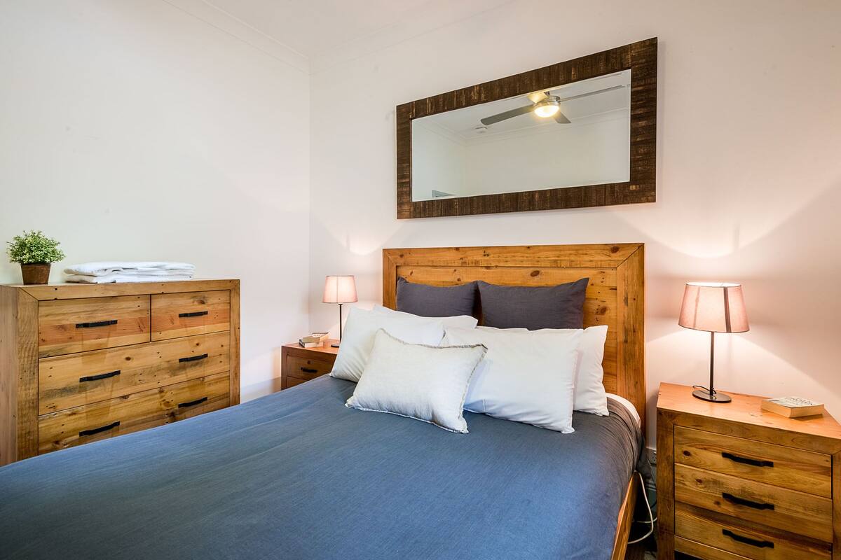 A neatly made bed with a blue bedspread, wooden headboard, and two bedside lamps.