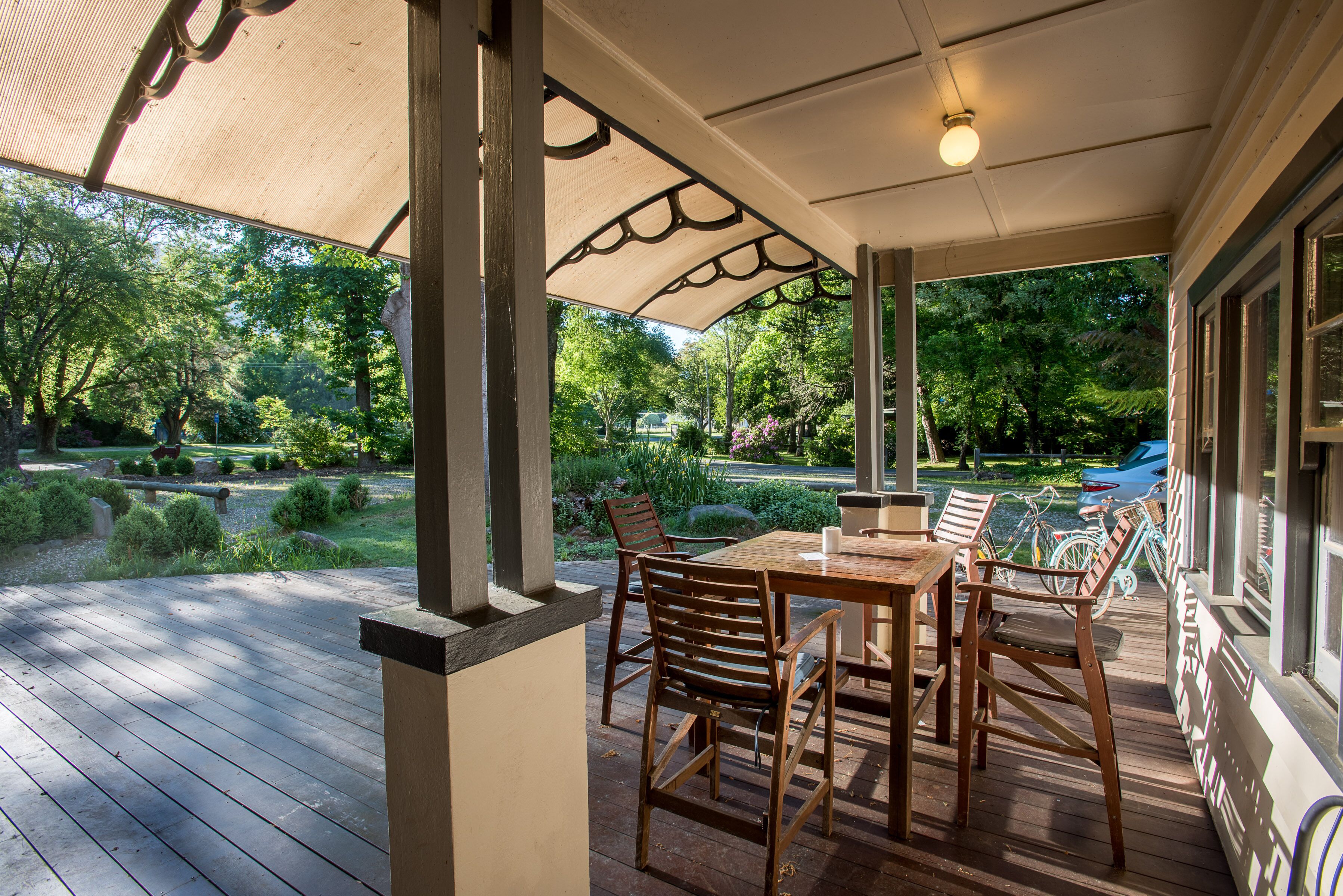 An outdoor patio with a wooden table and chairs, surrounded by a covered area with a view of a garden and a blue slide.