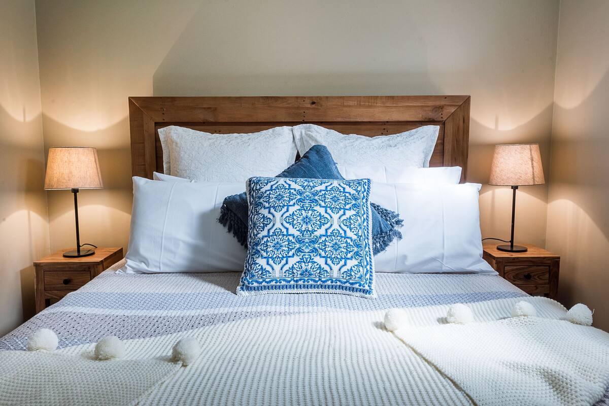 A neatly made bed with a patterned pillow, two bedside tables with lamps, and a wooden headboard.
