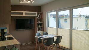 A modern kitchen with a built-in TV, a dining area with a table and chairs, and large windows with blinds. - Nice apartment in Graal-Müritz with WiFi (Graal-Müritz)