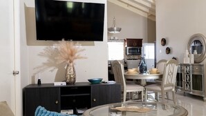 Un salon moderne doté d’un téléviseur à écran plat, d’une table basse en verre et d’un coin repas agrémenté d’un lustre.