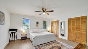 Ein Schlafzimmer mit Bett, Deckenventilator, Nachttisch, Stuhl, Fenster, Tür und Kleiderschrank.