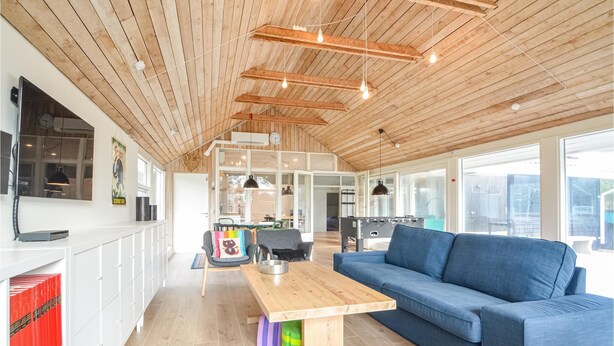 A spacious living area with a wooden ceiling, a blue sofa, a wooden coffee table, and a kitchen area visible through an open door. - 4 bedroom beautiful home in Vestervig (Vestervig)