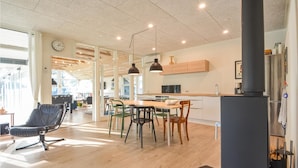 A modern kitchen with wooden cabinets, a dining table with chairs, and a large window providing natural light. - 4 bedroom beautiful home in Vestervig (Vestervig)