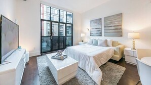 A modern bedroom with a large bed, a TV, a desk, and a balcony with a city view. - Santana Row Properties #7 - Silicon Valley Getaway (San Jose)