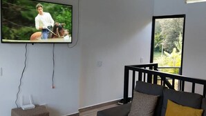 Un soggiorno moderno con una TV a parete, un divano grigio con cuscini, un tavolino e una finestra vista verde.