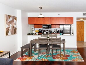 A modern kitchen with wooden cabinets, stainless steel appliances, and a dining area with a floral rug. - Brickell 1BR with Bay Views & Free Parking (Miami)