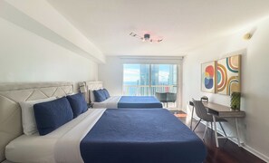 A hotel room with two beds, a desk, and a balcony with a city view.