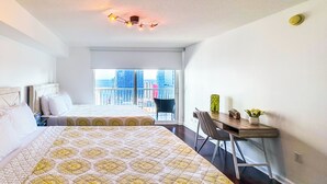 Hotelkamer met twee bedden, een bureau met stoel, een bijzettafeltje met vaas en uitzicht op de stad door grote ramen.