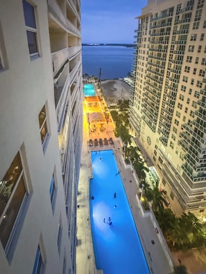 A swimming pool with people, surrounded by buildings and a view of the sea.