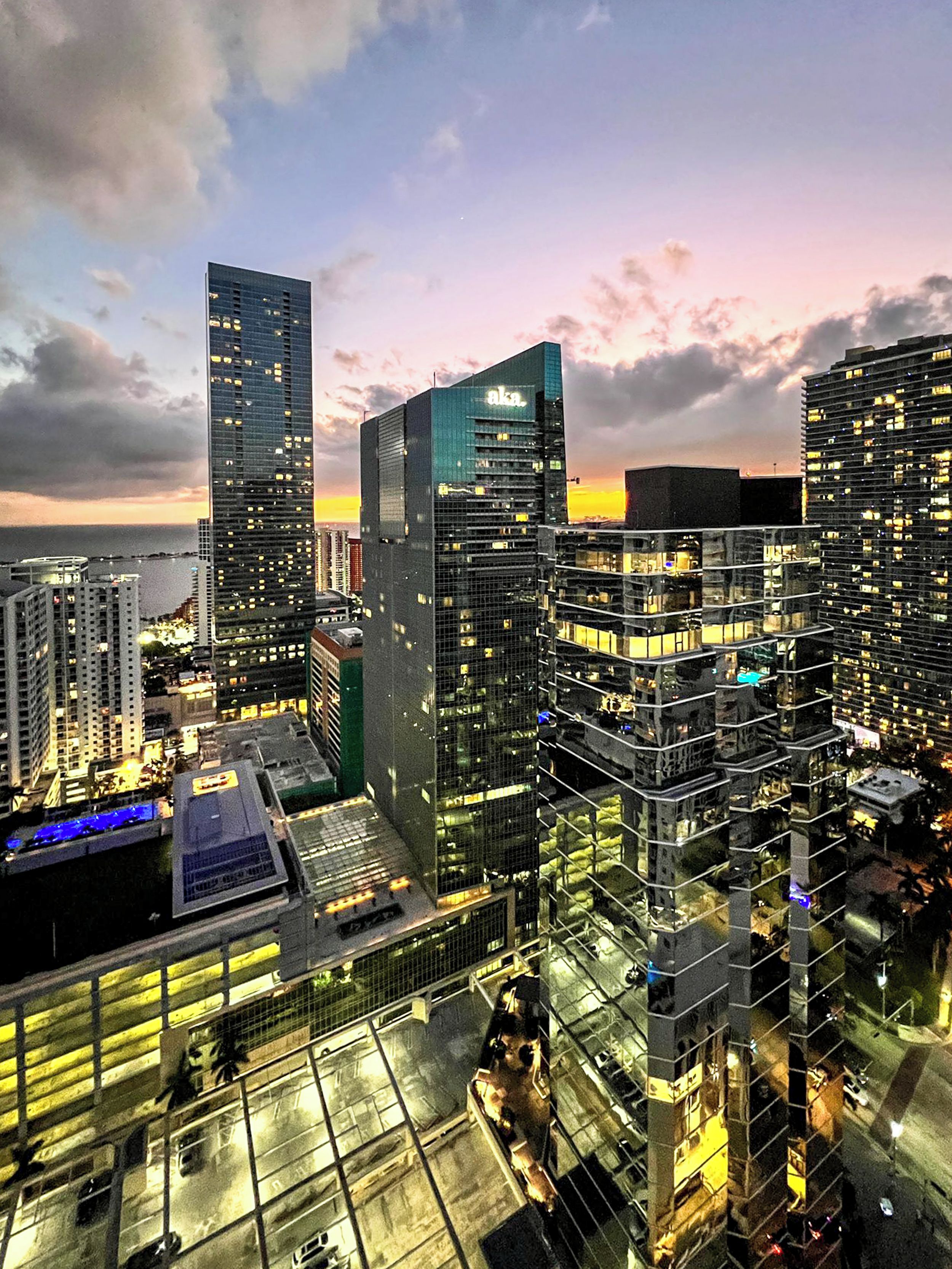 A high-rise urban area with modern buildings, a waterfront, and a sunset sky.