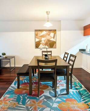 Un comedor con una mesa, sillas, un banco, un tapete estampado, una lámpara de pared y un adorno mural.