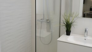 A modern bathroom with a glass-enclosed shower, a white sink, and a potted plant.