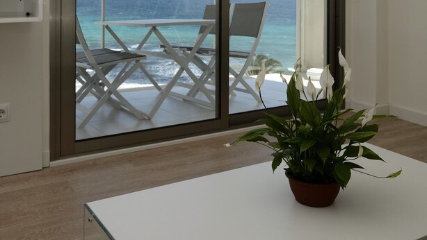 A balcony with a view of the ocean, a white table, and a potted plant.