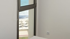 A room with a bed, a window with a view of the ocean, and a white wall.