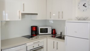 A modern kitchen with white cabinets, a microwave, a coffee maker, and a refrigerator.