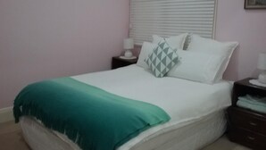 Une chambre à coucher avec un lit, une table de chevet, une lampe et une fenêtre avec des stores.
