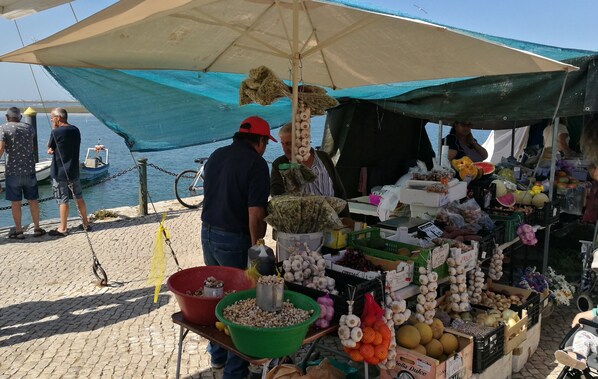 A market stall with various fruits and vegetables, including melons and onions, under a large umbrella.