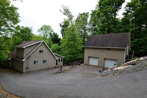 A two-story house with a garage, surrounded by trees and a gravel driveway.