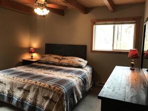 A bedroom with a bed, two bedside lamps, a window, and a wooden dresser.